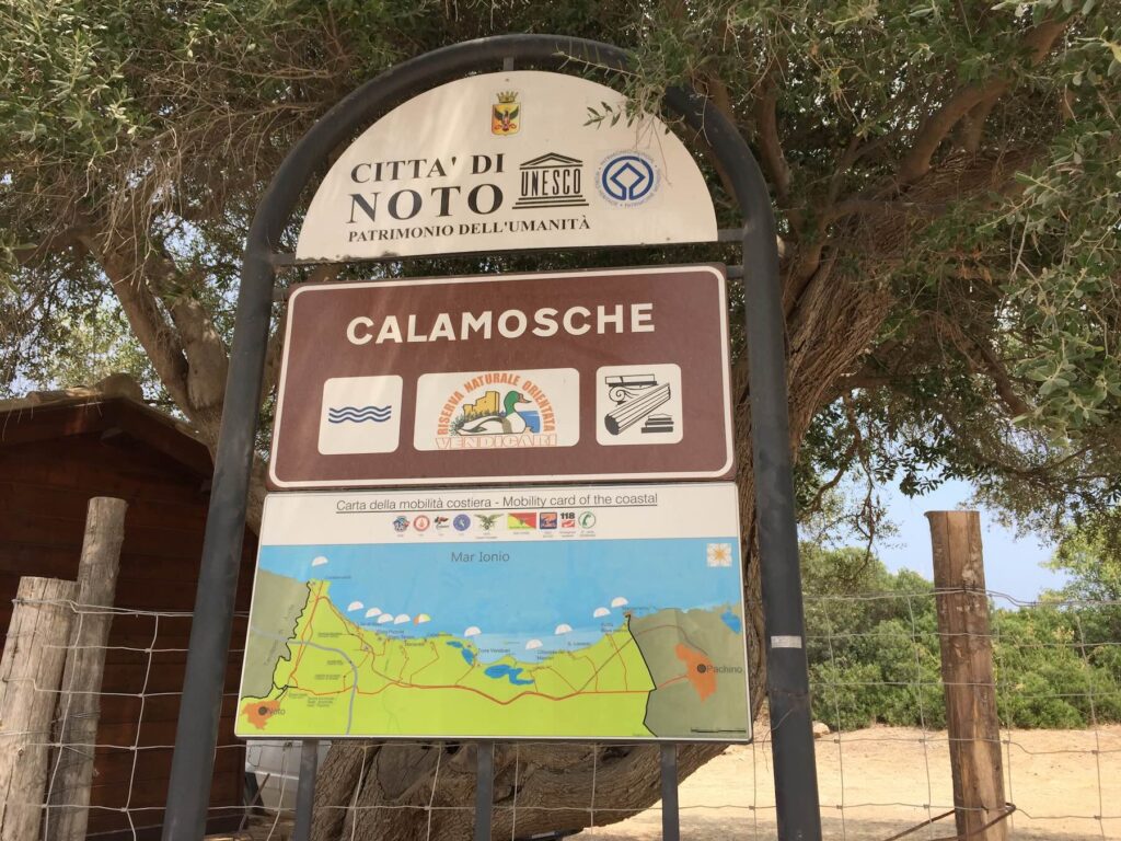 Cartello all’ingresso della spiaggia di Calamosche, con il logo della Riserva Naturale di Vendicari e della Città di Noto, sito patrimonio UNESCO.